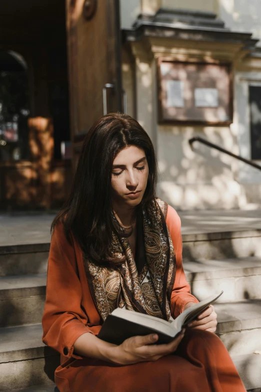 a young woman sits on the steps outside of a building reading a book