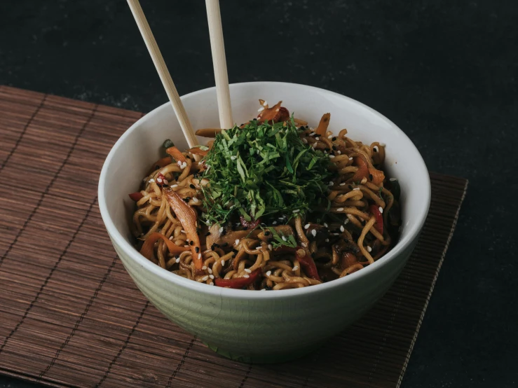 a bowl of noodles with vegetables and chop sticks on top of a placemat