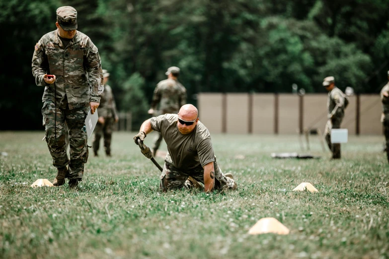 soldiers stand on the grass as one soldier kneels down