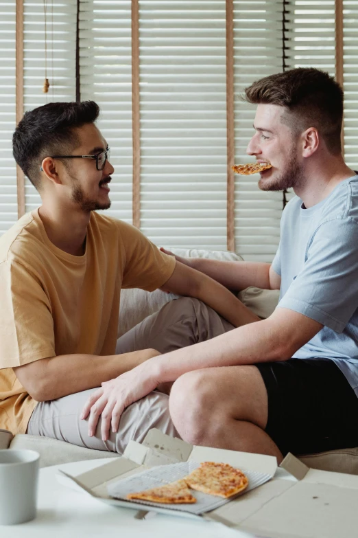 two men enjoying pizza while sitting together on the couch