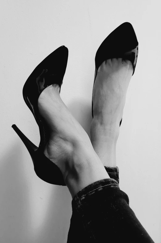 a woman's black high heeled shoes with her legs up against the wall