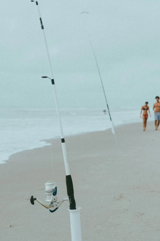 two people walking on the beach with a white fishing pole