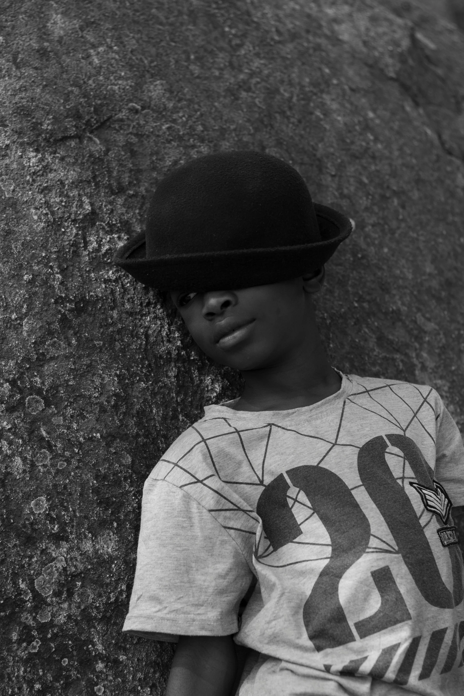 a young child wearing a fedora leaning against a rock