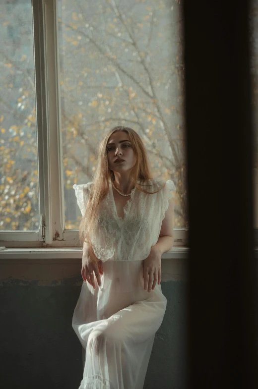 a woman wearing white dress sitting on ledge in front of a window