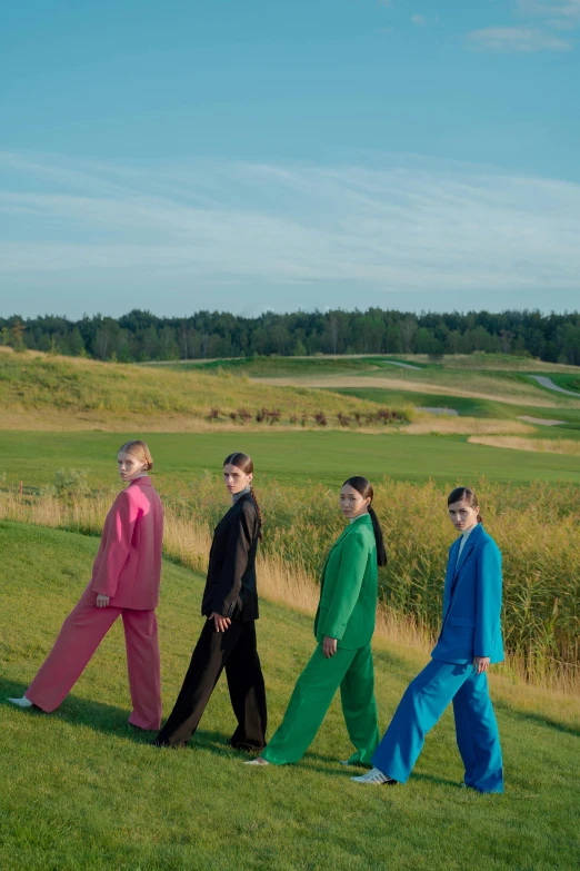 four people are walking in the grass wearing a group of three outfits