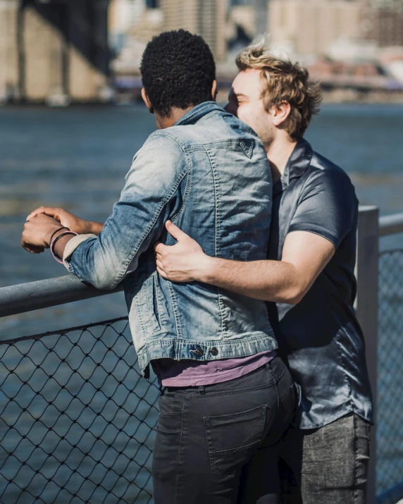 a man and woman hugging on a bridge overlooking water