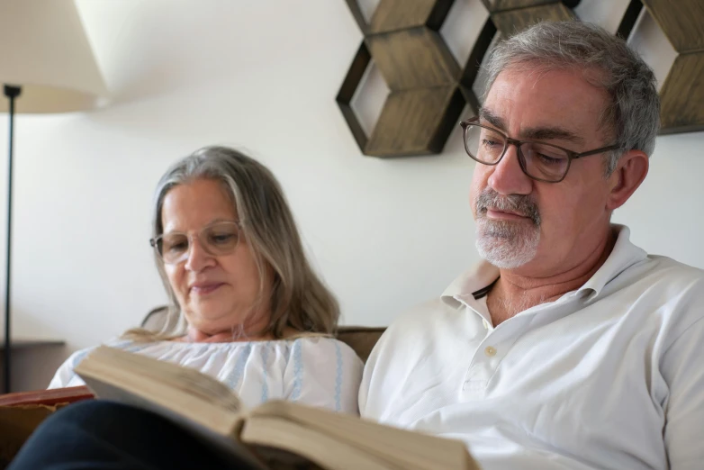 a woman sitting next to a man reading a book