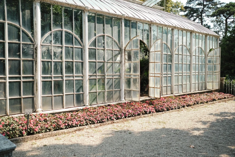 an ornate glass house in a park with many flowers