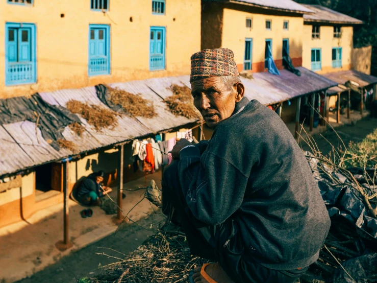 an older man kneeling in the dirt near houses