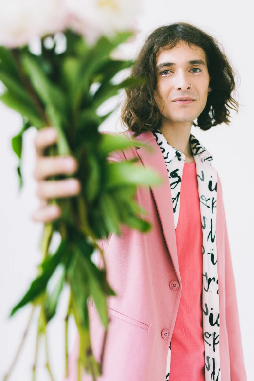 a woman is holding a pink coat next to a plant