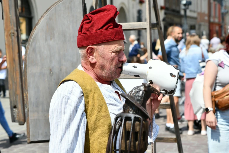 an old man with a red hat on his head drinking from a bull horn