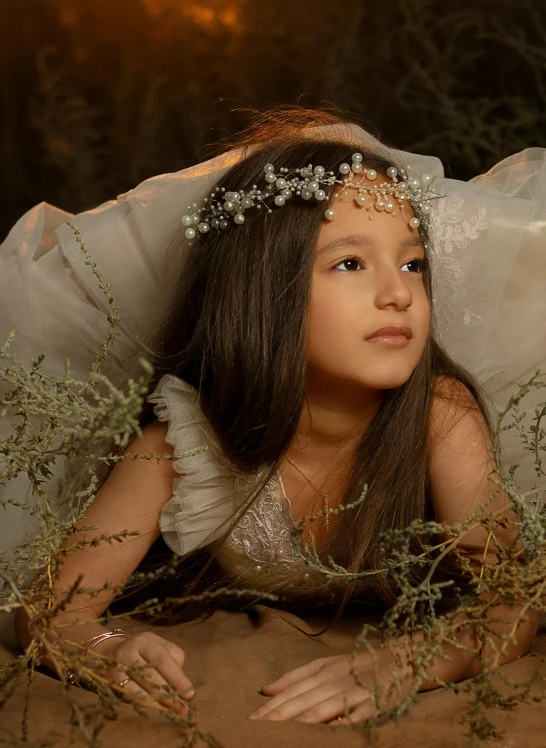 a beautiful little girl dressed in a white and gold dress laying down with her head tilted back