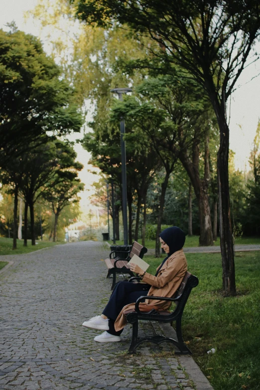 a woman in a hat sits on a bench near a park