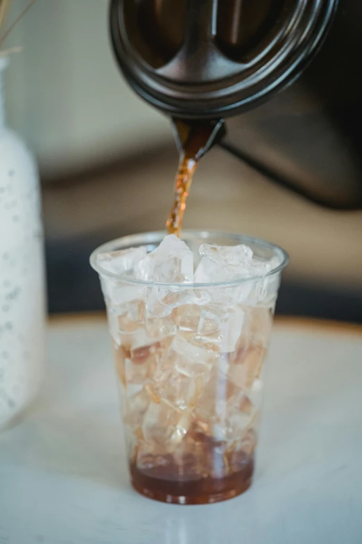 a person pouring tea into a glass with ice cubes