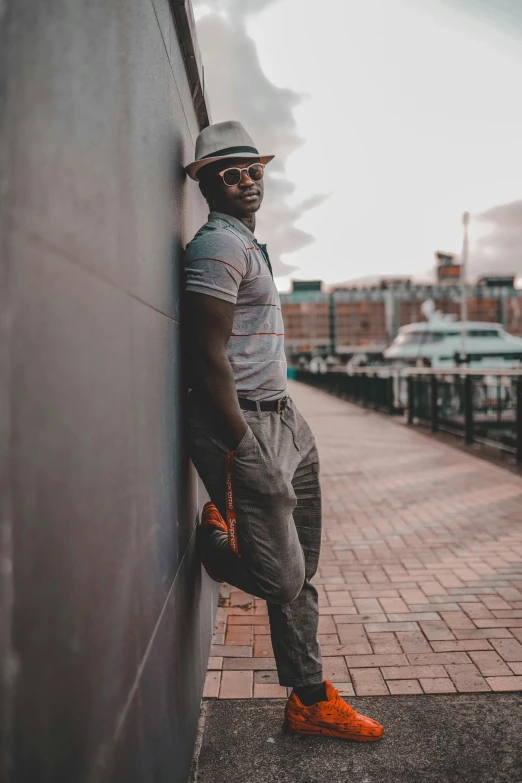 a young black man leans against a brick wall