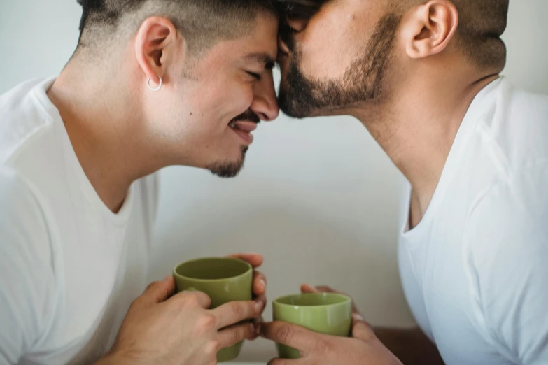 two young men sharing a kiss with cups