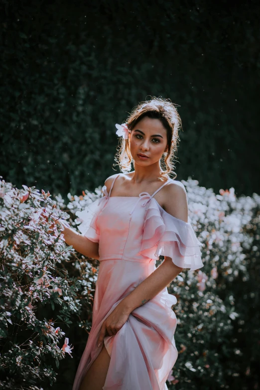 a woman in a pink dress standing near a bush