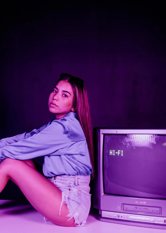 woman with legs crossed posing beside television, against purple background