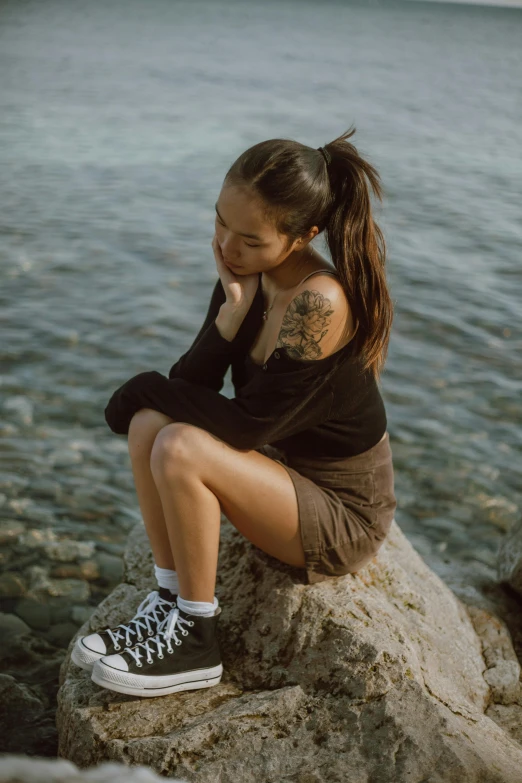 young woman sitting on rock near body of water