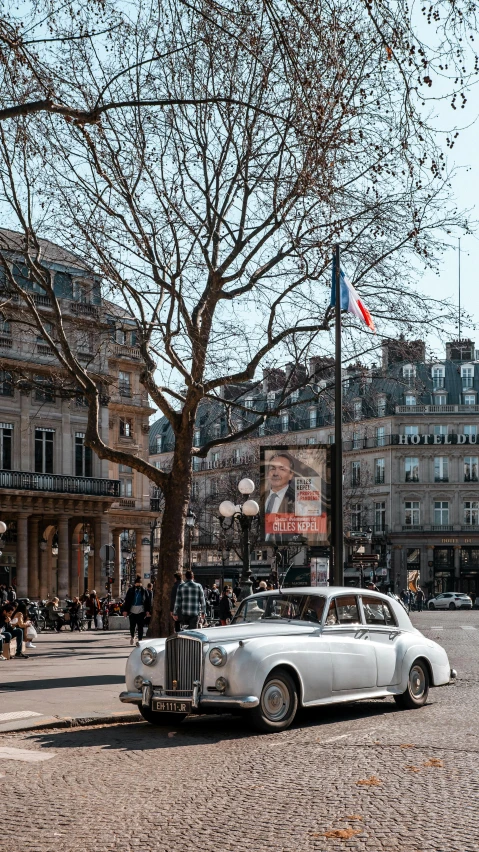 an old white car sits in the middle of a street