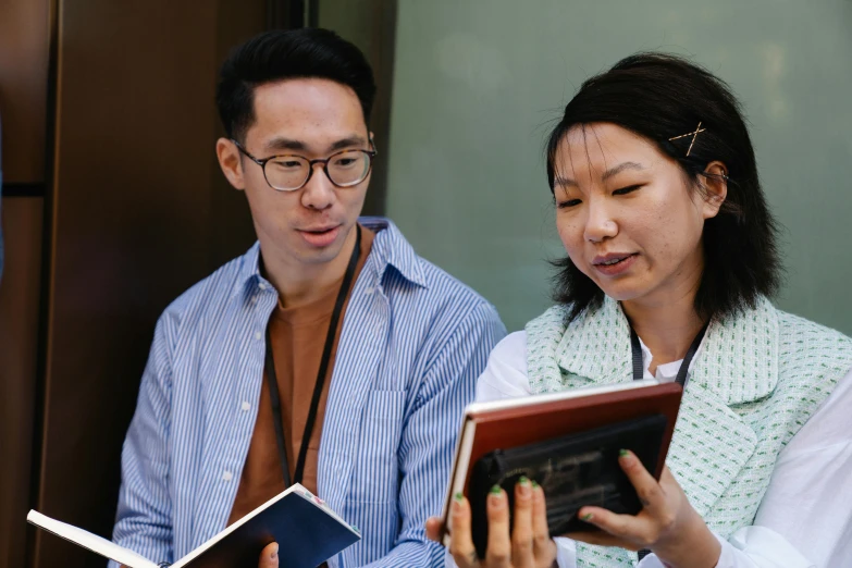 a couple of people standing next to each other looking at a book