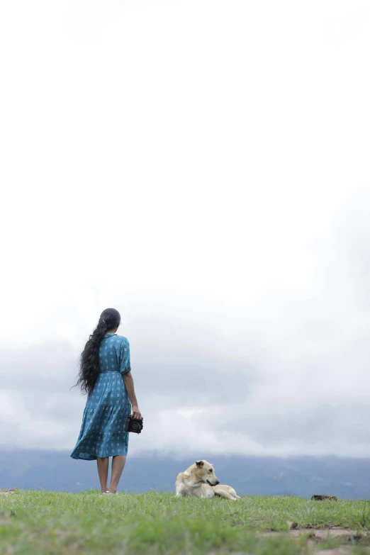 a woman in a blue dress walking her dog down a hill