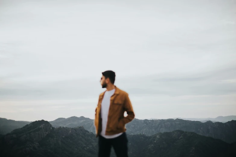 the man standing on a hill is wearing a jacket and black pants