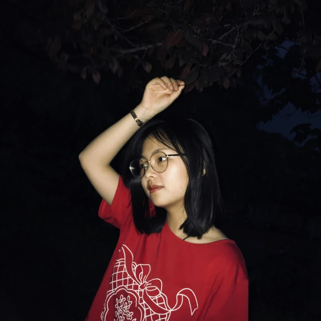 a woman in a red t - shirt and a black hat stands under a tree