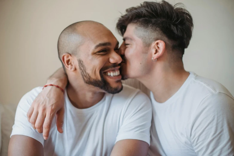 two young men one is kissing the other while they smile