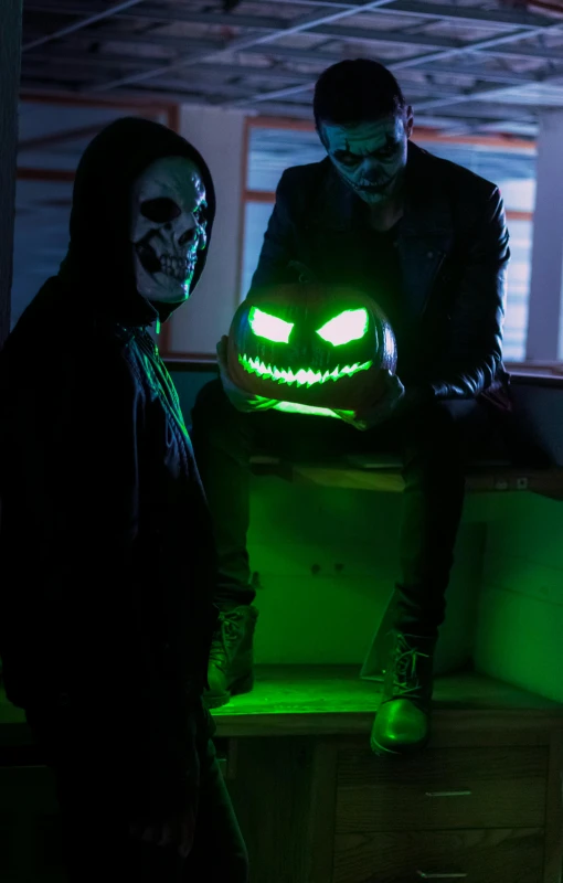 a person wearing a scary mask next to a glowing pumpkin in a dark room