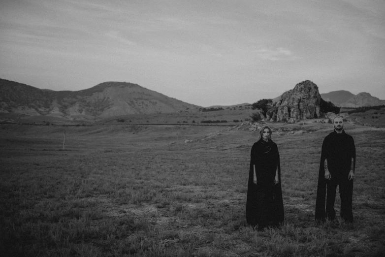 two people are standing in a field with mountains in the background