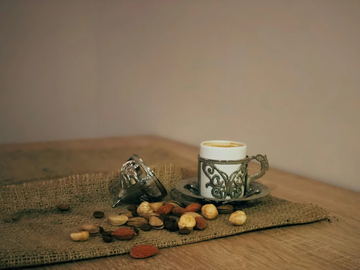 the coffee cup is on a wooden table next to nuts