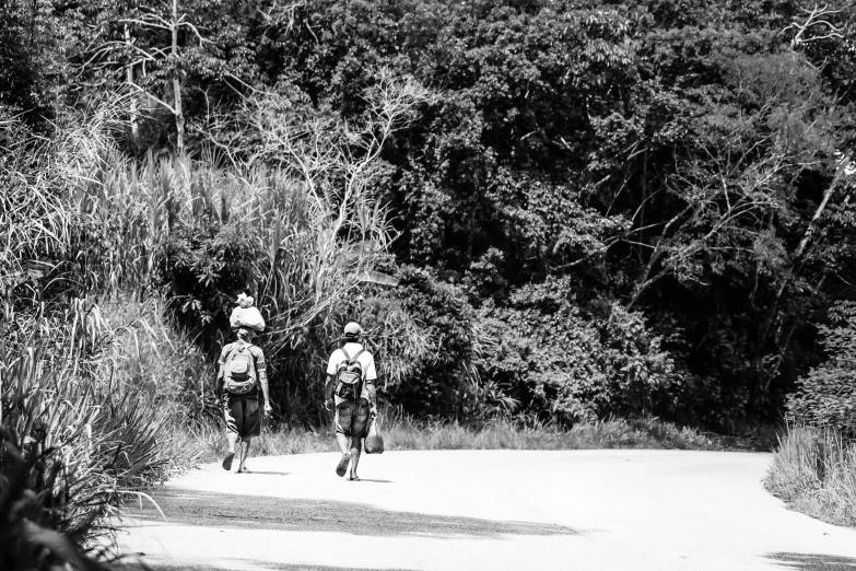 two people with backpacks walk down a gravel road