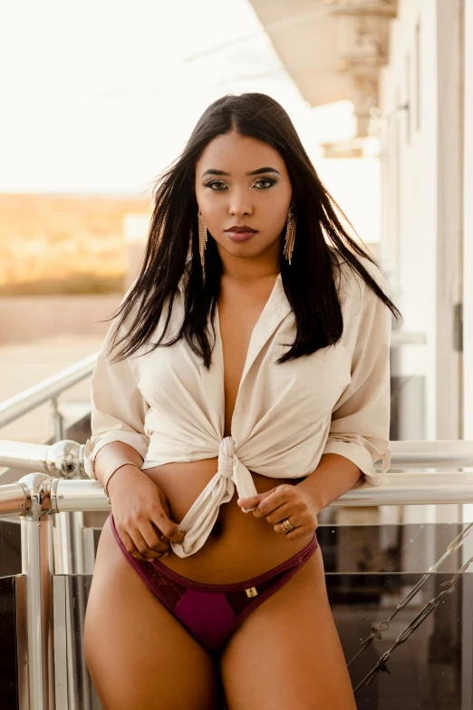 a black woman in a lingerie poses on the railing of a building