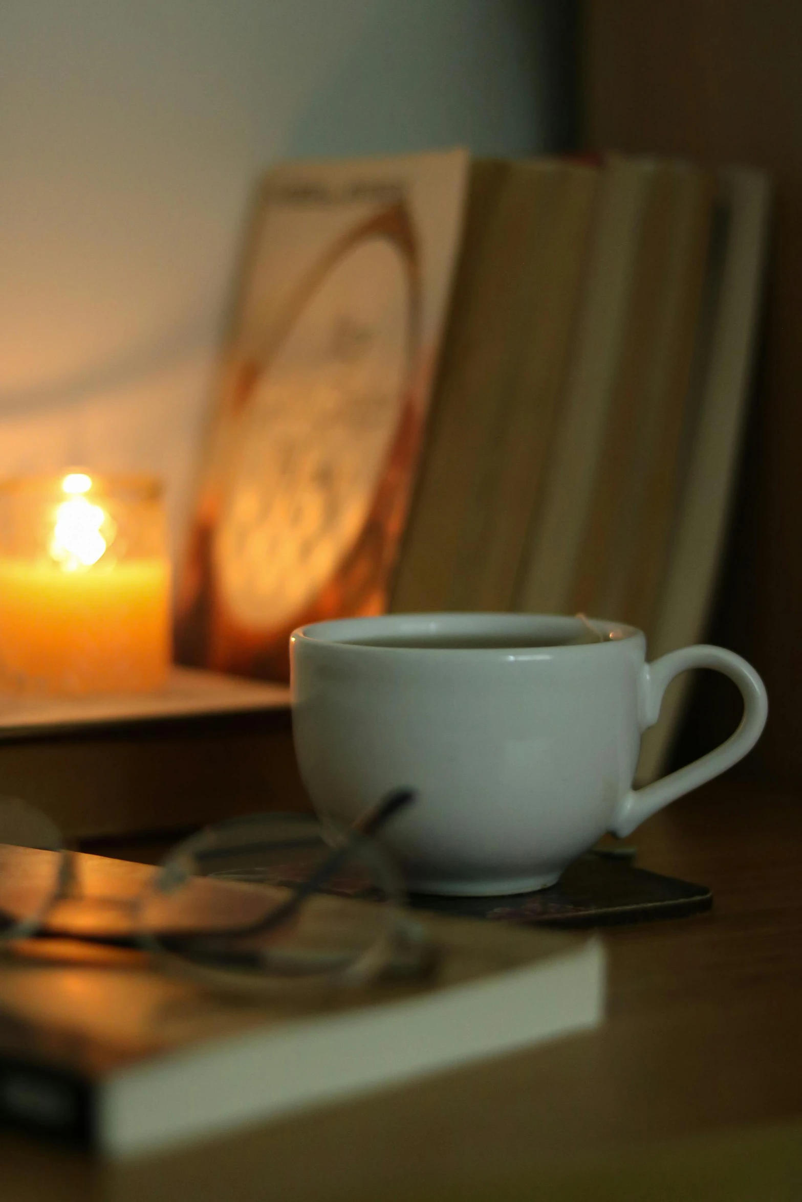the teacup is beside some books, a candle, and a book