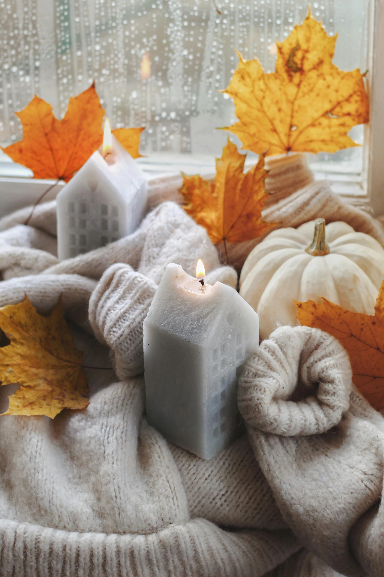 a candle that is surrounded by knits and fall leaves