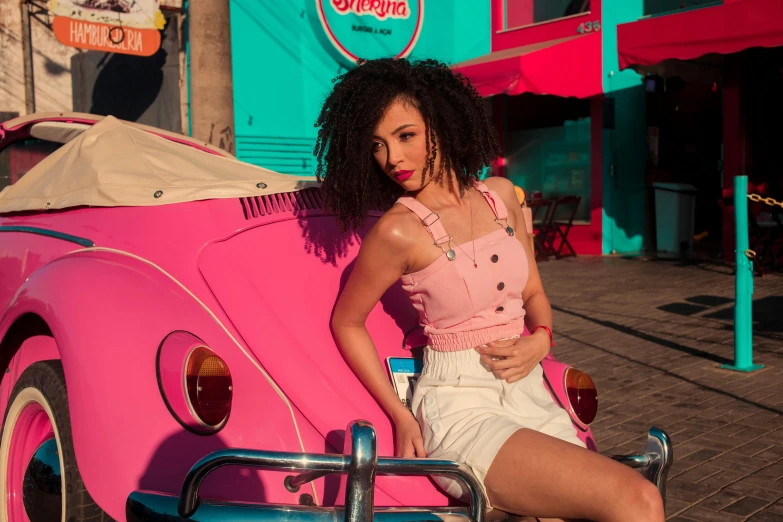 a woman leaning on a pink car in front of pink and blue buildings