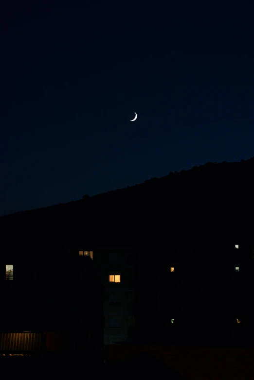 the moon rises in a dark sky over houses