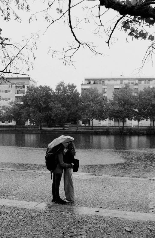 two people standing by the water under umbrellas