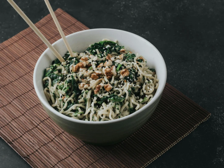 a bowl with noodles, greens and nuts in it