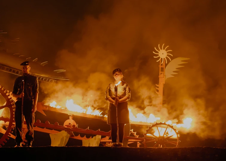 two men standing in front of a huge pile of fire