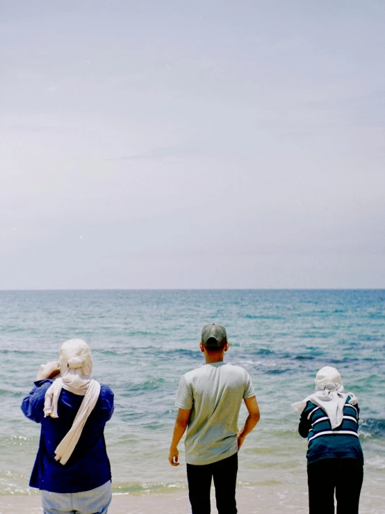 three people standing in front of the ocean