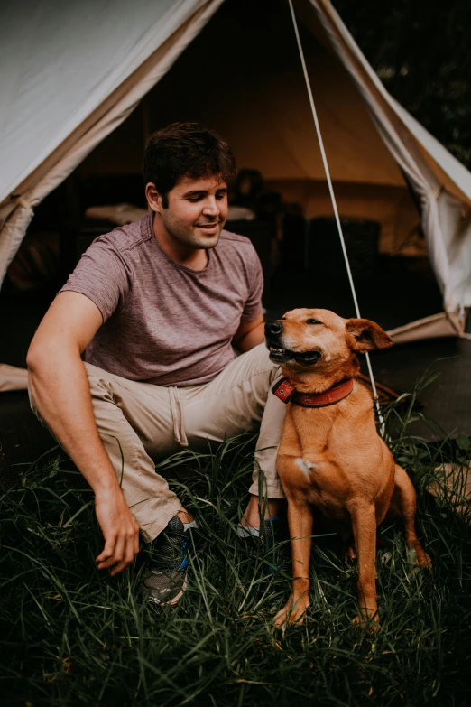 a man and his dog are sitting in the grass outside of their tent