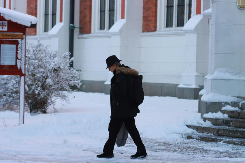 a man walking on a snowy sidewalk in front of a red phone booth