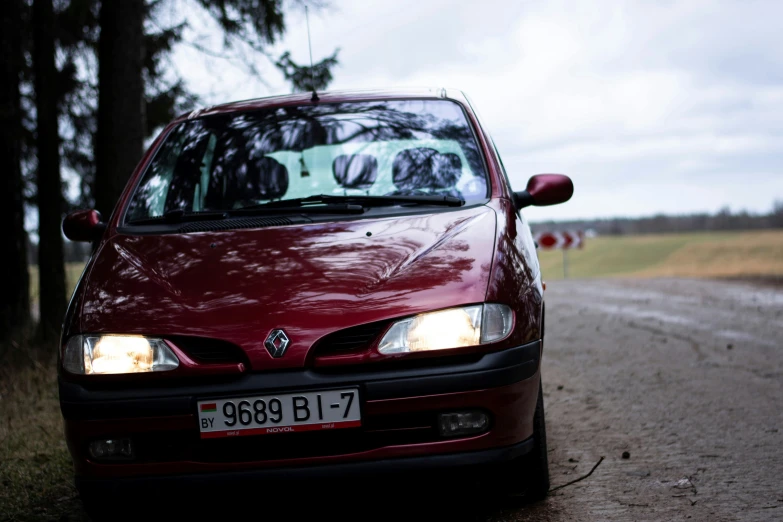 the red car is parked along the gravel road