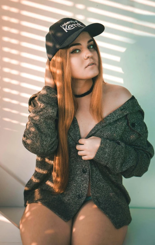 a woman sitting against a wall while wearing a hat