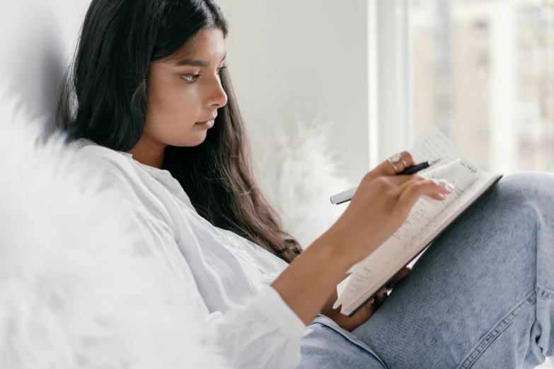 a young woman sits reading a note pad with an ink pen in her lap