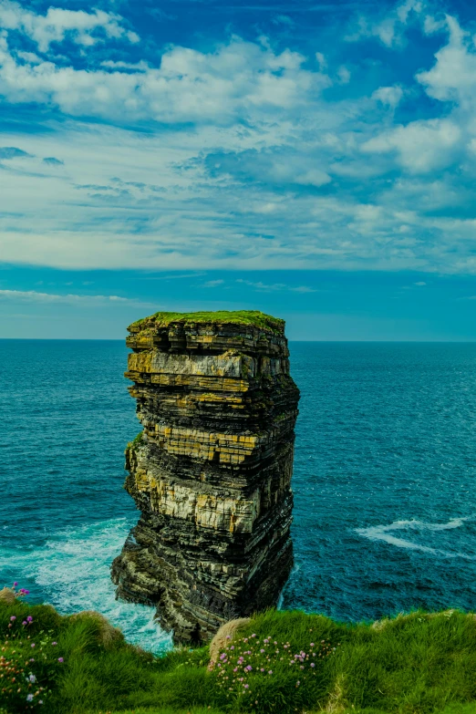 a rocky cliff on the coast with a lone boat floating by