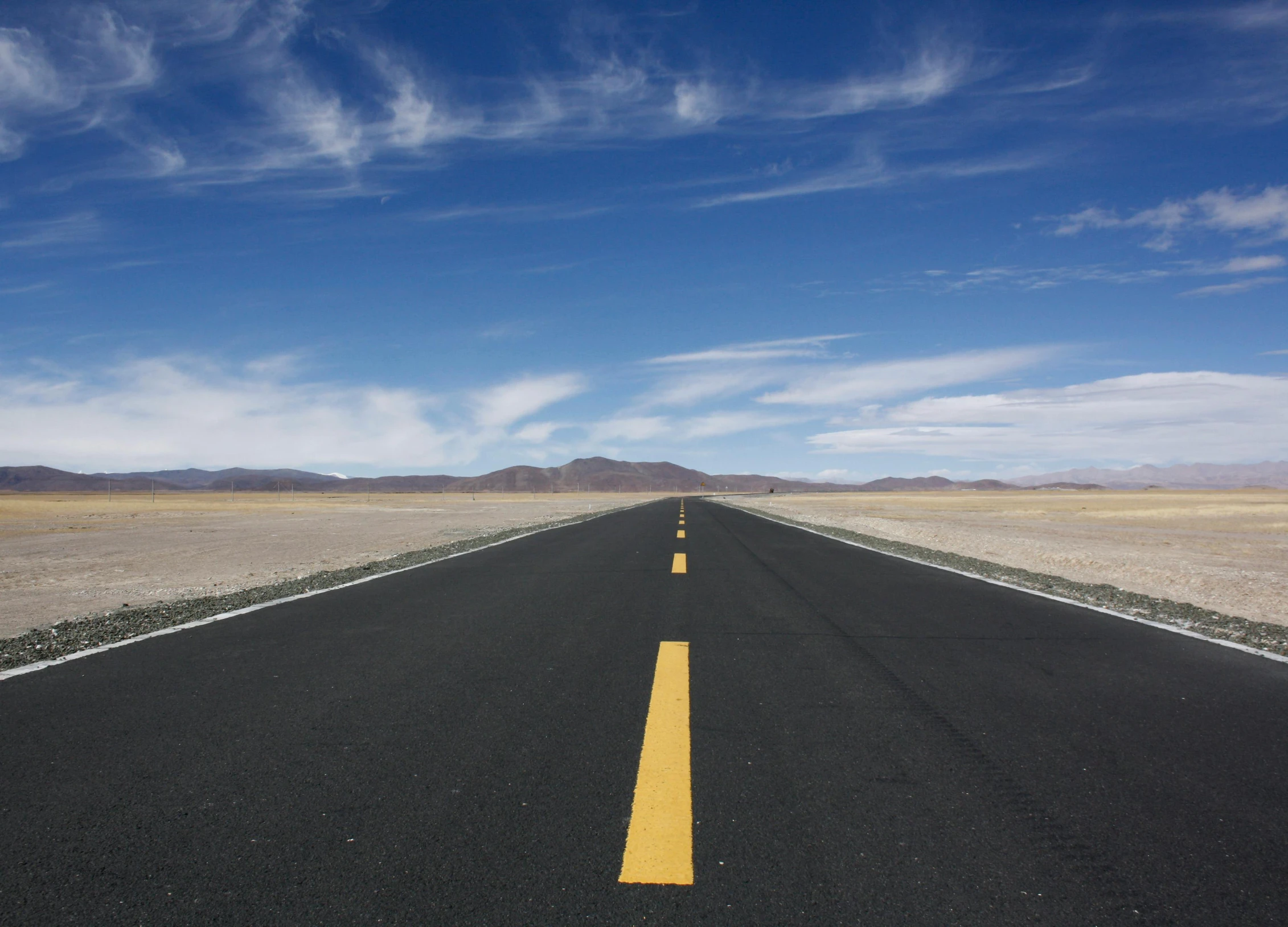 an empty highway is shown with mountains in the background