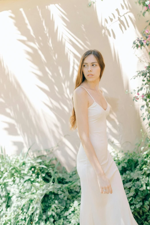 a woman is standing in the shade, she is wearing a long white gown